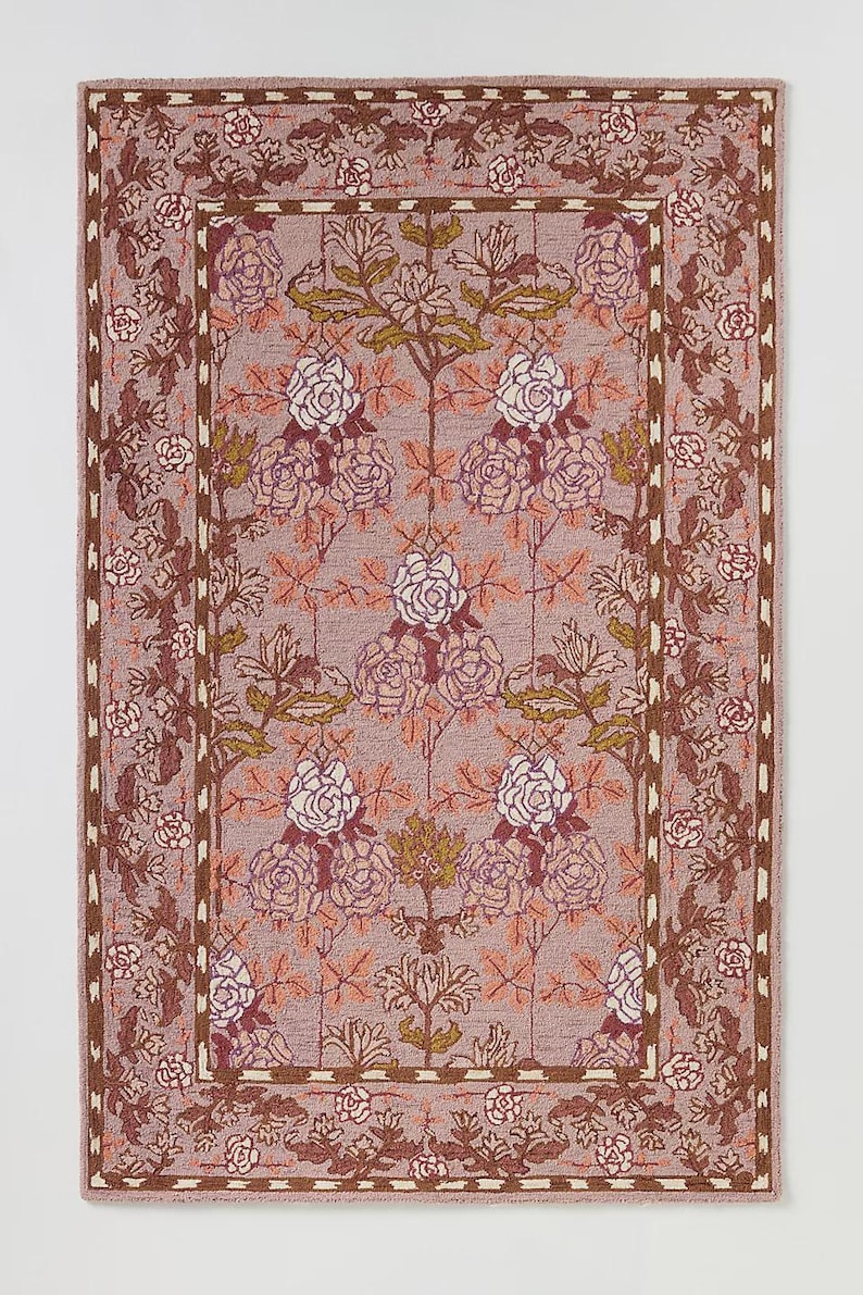 May include: Rectangular rug with a floral pattern in shades of mauve, brown, and cream. The design features stylized roses and foliage, framed by a border with repeating floral motifs. The rug's color palette is muted and elegant.