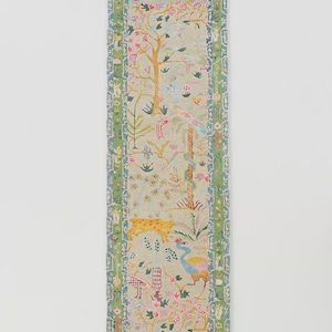 May include: A rectangular, decorative runner featuring a whimsical, colorful design. The runner showcases a light beige background with a detailed pattern of trees, flowers, birds, and a leopard. The edges are bordered with a green and blue floral pattern.