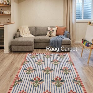 May include: A rectangular rug with a floral pattern. The rug features a cream background with blue vertical stripes and repeating floral motifs in red and green. The border is red. The rug is placed on a light wood floor.