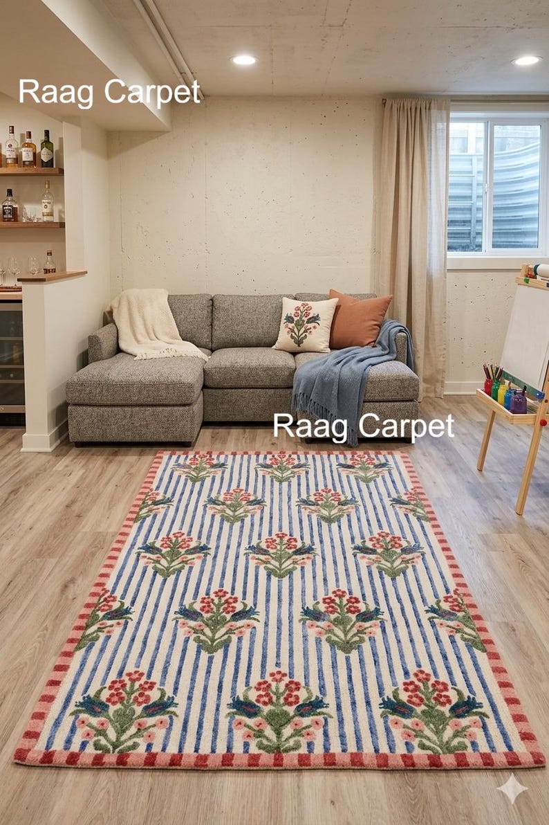 May include: A rectangular rug with a floral pattern. The rug features a cream background with blue vertical stripes and repeating floral motifs in red and green. The border is red. The rug is placed on a light wood floor.