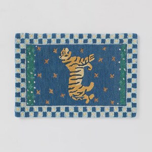 Op de afbeelding: Blauw rechthoekig tapijt met een tijgermotief. De tijger is geel en zwart, tegen een blauwe achtergrond met gouden sterren. Het tapijt heeft een blauw-witte geblokte rand.