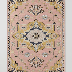 May include: A rectangular rug with a pink background and a detailed geometric pattern. The design incorporates yellow, navy, and white floral and geometric shapes. The rug has a border with a repeating pattern.