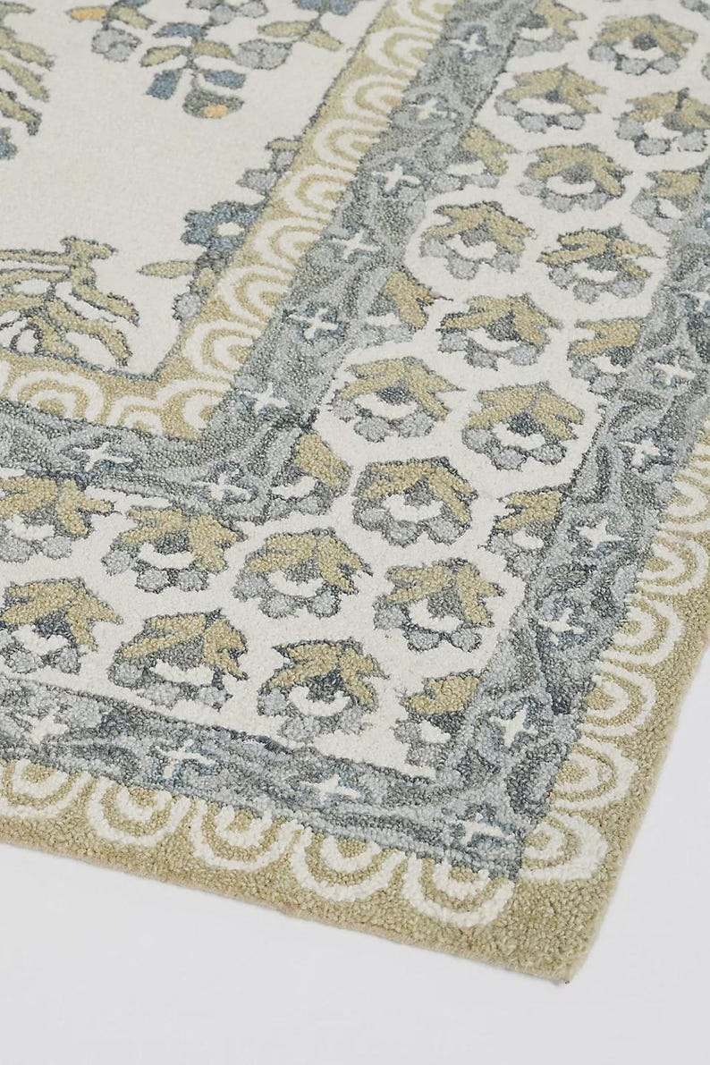 May include: A rectangular rug with a floral pattern in shades of cream, gray, and gold. The rug features a detailed border with a repeating floral motif and a scalloped edge. The design is symmetrical and creates a classic, elegant look.