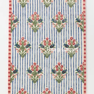 May include: Rectangular rug with a blue and white striped background. The rug features a repeating floral pattern in pink, green, and blue. The border is a red and pink striped pattern. The text "Raag Carpet" is visible.