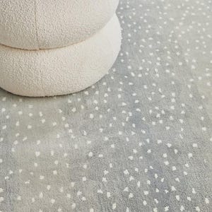 May include: A light gray rug with a speckled pattern and a white, round, two-tiered ottoman. The rug has a soft, textured appearance, and the ottoman is made of a plush, cream-colored material. The overall aesthetic is modern and minimalist.