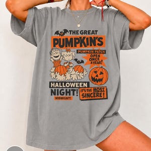 Könnte beinhalten: Ein graues Kurzarm-T-Shirt mit einem Grafikdruck mit dem Text THE GREAT PUMPKIN'S PUMPKIN PATCH OPEN ONCE A YEAR! HALLOWEEN NIGHT! MIDNIGHT! IT'S THE MOST SINCERE! sowie Illustrationen von zwei Zeichentrickfiguren und Kürbissen.