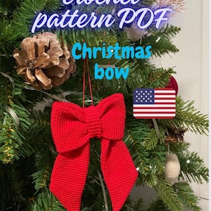Peut inclure: Une décoration de Noël en forme de nœud rouge crocheté suspendue à un sapin de Noël vert. L'ornement est fait avec un fil rouge et a une forme de nœud classique. Le texte "crochet pattern PDF Christmas bow" est visible en haut de l'image.