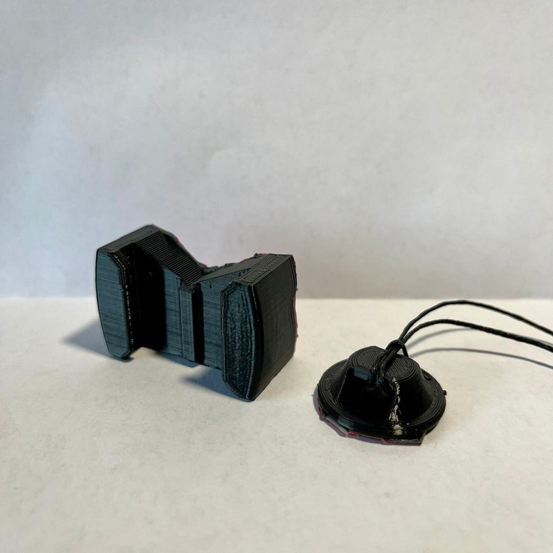 May include: A 3D printed black plastic camera mount with a small black plastic disc and a black string attached.