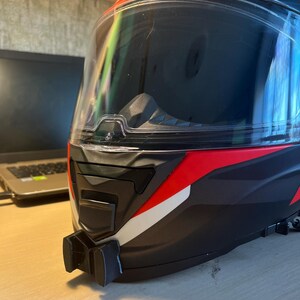 May include: A black and red motorcycle helmet with a clear visor and a white stripe. The helmet has a GoPro mount attached to the bottom.