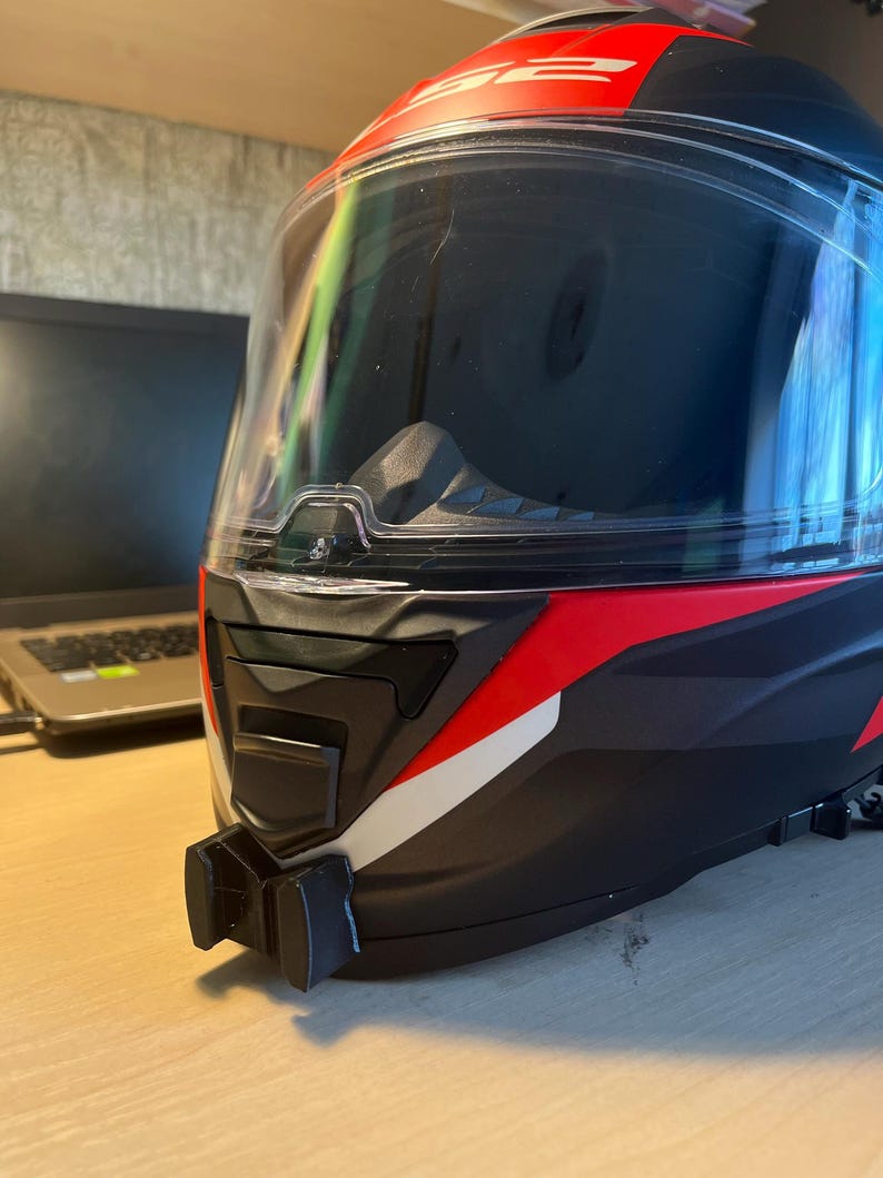 May include: A black and red motorcycle helmet with a clear visor and a white stripe. The helmet has a GoPro mount attached to the bottom.