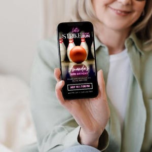 A person is holding up a smartphone displaying an invitation for a bowling-themed birthday party.