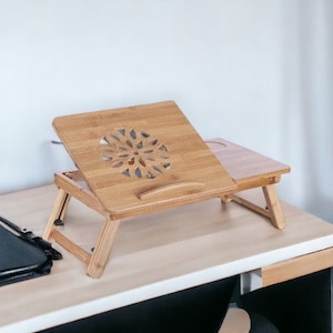 May include: A wooden laptop stand with a cutout design in the shape of a flower. The stand is folded up and sitting on a white table.