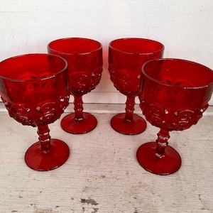 May include: Four red glass goblets with a textured, raised design. The goblets have a round bowl and a tall stem.