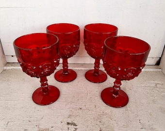 May include: Four red glass goblets with a textured, raised design. The goblets have a round bowl and a tall stem.