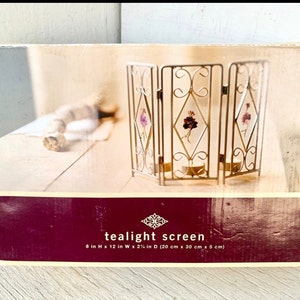 May include: A gold metal tealight screen with a decorative floral design. The screen is 8 inches high, 12 inches wide, and 2 1/2 inches deep.
