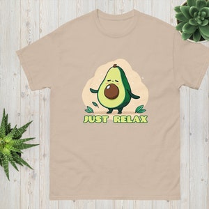 Puede incluir: Una camiseta de color beige con un aguacate de dibujos animados con una expresión relajada y el texto "JUST RELAX".