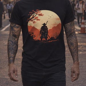 May include: Black t-shirt featuring a samurai warrior graphic in a circular design with a red and orange sunset backdrop. The person is wearing black jeans and has tattoos on both arms.