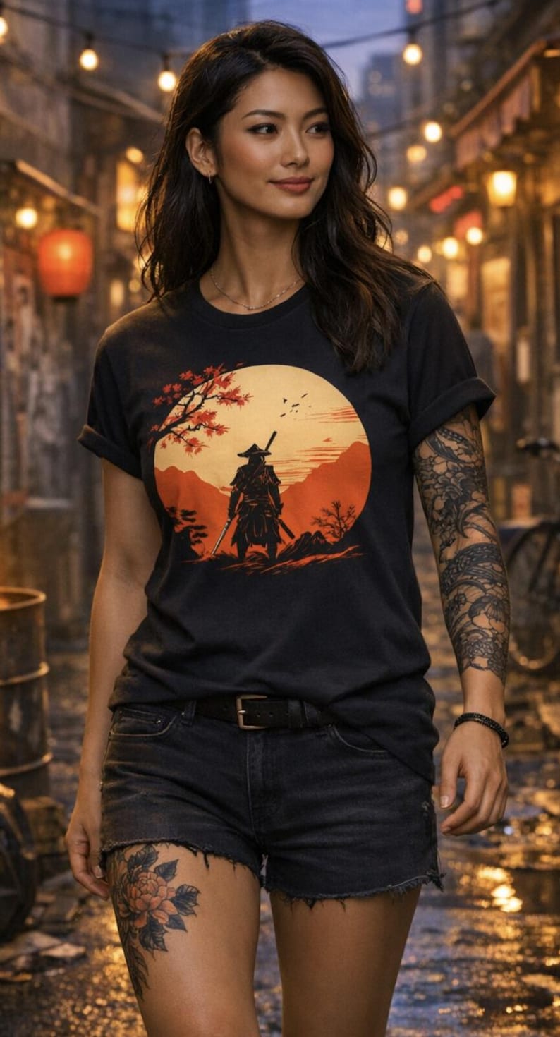 May include: Black t-shirt featuring a graphic of a samurai warrior standing in a landscape with a large orange sun. The design includes a tree with red leaves. The person is wearing black shorts and has a tattoo on their arm and leg.