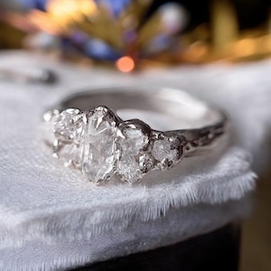 Puede incluir: Un anillo de plata con un grupo de diamantes blancos en bruto engastados en una banda texturizada.