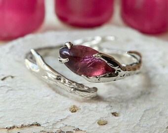 May include: A silver ring with a branch design and a pink gemstone. The ring is open and adjustable.
