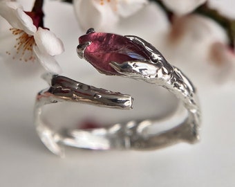 May include: A silver ring with a pink gemstone set in a branch-like design.