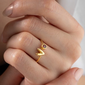 May include: Gold ring with a red gemstone and a V-shaped design.
