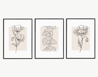 Puede incluir: Conjunto de tres impresiones enmarcadas en negro con dibujos minimalistas de flores y hojas sobre un fondo beige. Las impresiones presentan una amapola, una hoja de ginkgo y otra amapola.