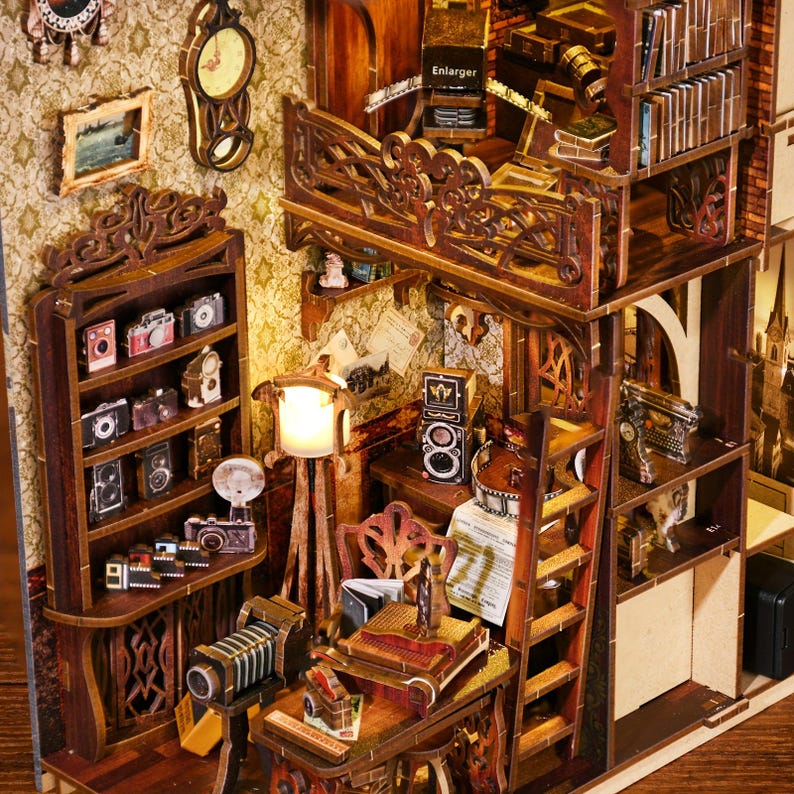 May include: A wooden miniature dollhouse with a detailed interior, featuring a bookshelf, a desk with a typewriter, a ladder, and a balcony with the word "Enlarger" printed on it.