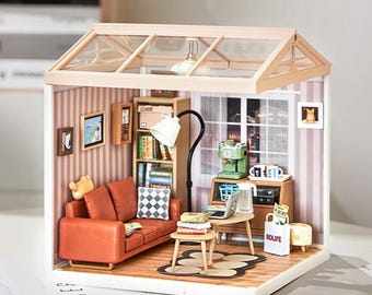 May include: A miniature dollhouse living room with a brown leather sofa, a coffee table with books, a lamp, a bookshelf, and a coffee maker. The dollhouse has a glass roof and is made of wood.