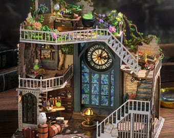 Könnte beinhalten: Ein Miniatur-Puppenhaus aus Holz mit einem skurrilen, gotischen Design. Das Puppenhaus verfügt über einen Uhrturm mit Buntglasfenstern, einen Balkon mit grünem Dach und eine Wendeltreppe. Der Innenraum ist mit Miniaturmöbeln und Accessoires dekoriert, darunter ein Kessel, Bücher und eine weiße Eule.