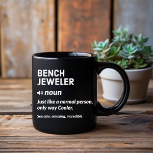 May include: Black coffee mug with white text that reads "BENCH JEWELER noun Just like a normal person, only way Cooler. See also: amazing, incredible"