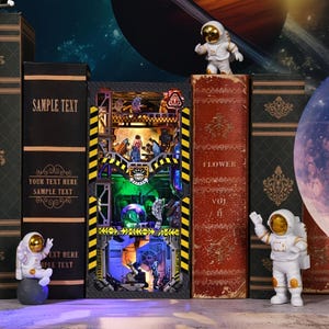 May include: A 3D model of a space station with a clear dome and a glowing blue light inside. The model is made of metal and plastic and is surrounded by books and astronaut figurines. The books have the words "SAMPLE TEXT" and "FLOWER" on their spines.