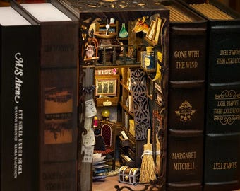 Könnte beinhalten: Detailliertes Diorama eines Miniaturzimmers, das in ein Buch geschnitzt wurde. Der Raum verfügt über Regale, einen Stuhl, eine Truhe und einen Besen. Die Buchrücken sind dunkelbraun mit goldfarbenen Buchstaben, darunter "GONE WITH THE WIND" und "MAGIC".