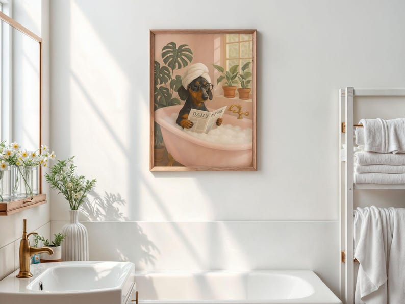 May include: A framed print depicts a dachshund in a pink bathtub, wearing a towel and glasses, reading a newspaper. The print has a wooden frame and is set against a pink wall with plants.