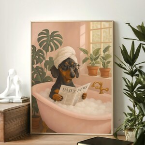May include: A framed print depicts a dachshund in a bubble bath, wearing a towel and glasses, reading a newspaper with "DAILY NEWS" printed on it. The dog is in a pink tub, with plants and a window in the background. The print has a light brown frame.