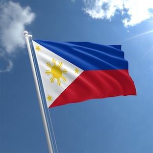 Puede incluir: La bandera de Filipinas ondea al viento. Es una bandera tricolor horizontal con una banda superior azul, una banda media blanca y una banda inferior roja. La banda blanca presenta un sol amarillo con ocho rayos y tres estrellas de cinco puntas.