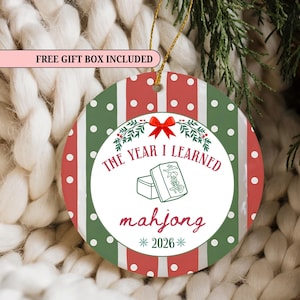 May include: A round ceramic Christmas ornament featuring a red and green striped pattern with white polka dots. The center displays a white circle with a red bow, a mahjong tile illustration, and the text THE YEAR I LEARNED mahjong 2026.