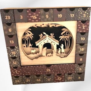 Puede incluir: Calendario de Adviento de madera con 24 cajones numerados. El centro presenta una escena de la Natividad cortada con láser con palmeras, ángeles y un establo. Los cajones están decorados con varios patrones y colores, incluyendo marrón, dorado y gris oscuro.
