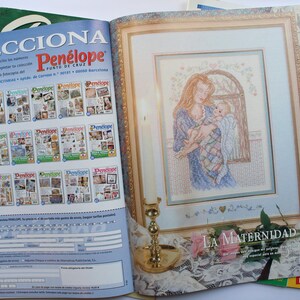 May include: A magazine cover featuring a cross-stitch pattern of a mother holding a baby. The title of the pattern is "La Maternidad" and the magazine is called "Pen&eacute;lope".