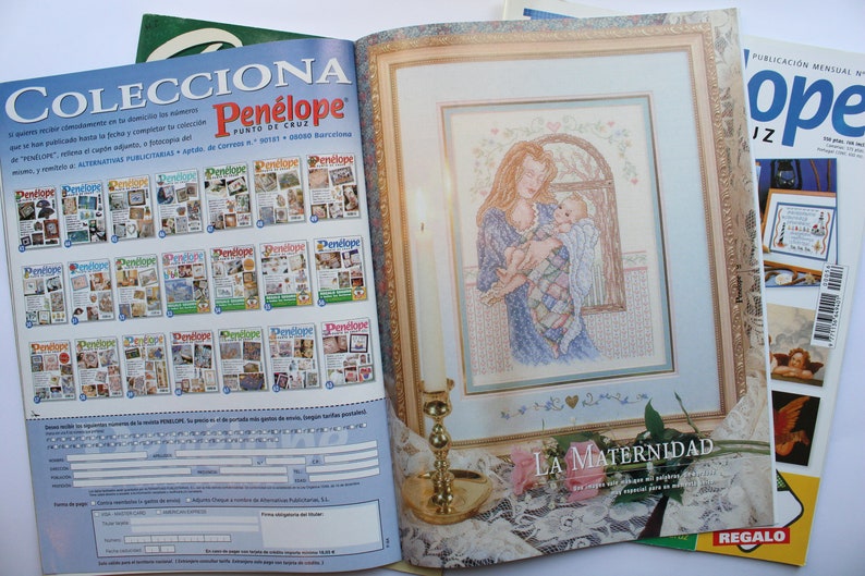 May include: A magazine cover featuring a cross-stitch pattern of a mother holding a baby. The title of the pattern is "La Maternidad" and the magazine is called "Pen&eacute;lope".