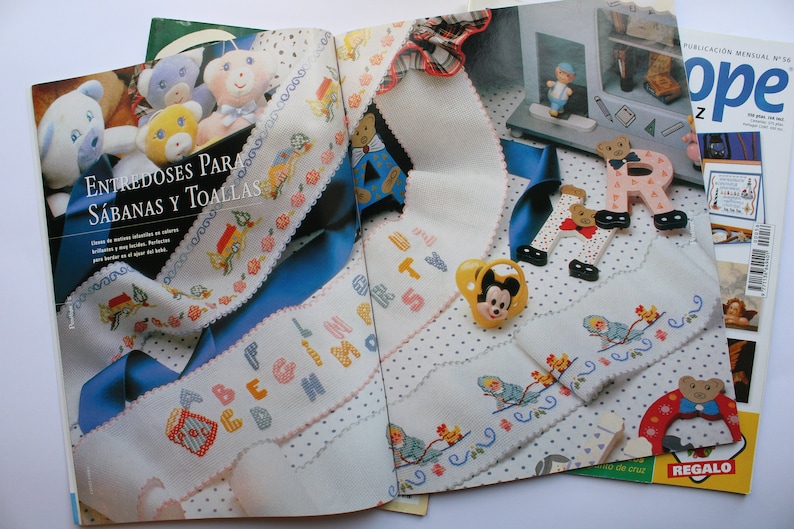 May include: An open magazine with a white background and colorful embroidery designs. The magazine cover features the word "Hope" in large, colorful letters. The magazine is titled "Entre doses para sabanas y toallas" and features a variety of embroidery patterns, including letters, animals, and flowers.