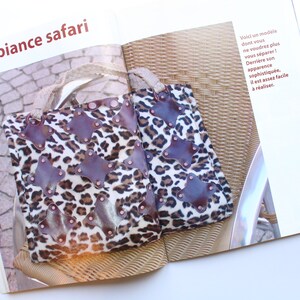 May include: Two leopard print tote bags with brown leather accents and metal studs. The bags are sitting on a wicker chair.