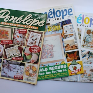 May include: Three copies of the Spanish language magazine "Pen&eacute;lope Punto de Cruz" featuring cross-stitch patterns. The magazine covers feature images of kitchen motifs, angels, and children.