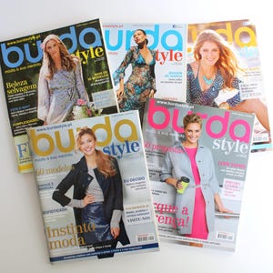 Op de afbeelding: Een verzameling van vijf Burda Style tijdschriften met verschillende omslagontwerpen. De tijdschriften tonen modellen, mode en het Burda Style logo. De covers tonen een reeks kleuren en stijlen, met tekst in meerdere talen.