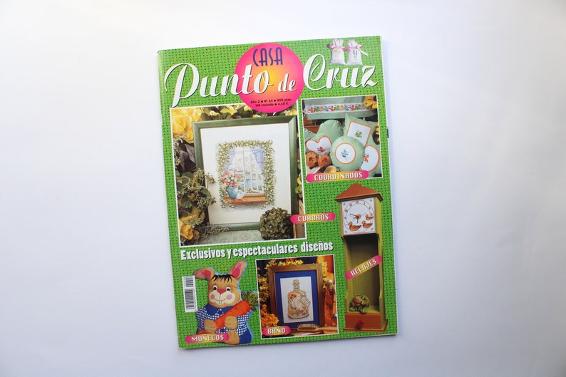 May include: A green magazine cover with the title "Casa Punto de Cruz" and images of cross-stitch designs, including a window, a clock, a bunny, and a bottle. The text "Exclusivos y espectaculares dise&ntilde;os" is at the bottom of the cover.