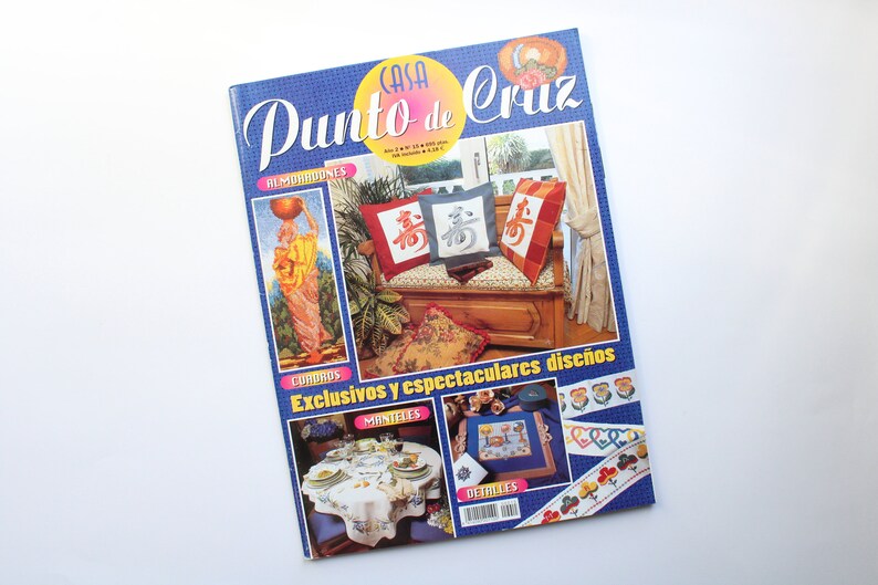 May include: A magazine cover featuring cross-stitch designs. The cover features a blue background with the title "Casa Punto de Cruz" in white lettering. The cover also features images of cross-stitch projects, including pillows, tablecloths, and borders.