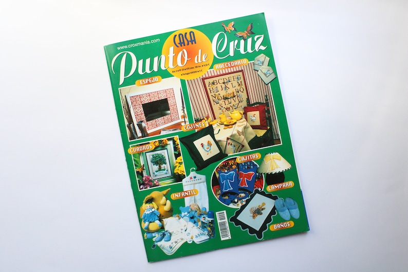 May include: A green magazine cover with the title "Casa Punto de Cruz" and images of cross-stitch projects, including a mirror, pillows, a lamp, and a pair of slippers.