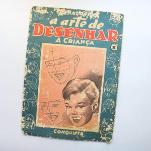 Pode incluir: Um livro vintage intitulado "A arte de Desenhar a Crianca" com uma capa azul e ilustrações de rostos. O livro faz parte de uma série, como indicado pelo numeral romano "II" na capa.