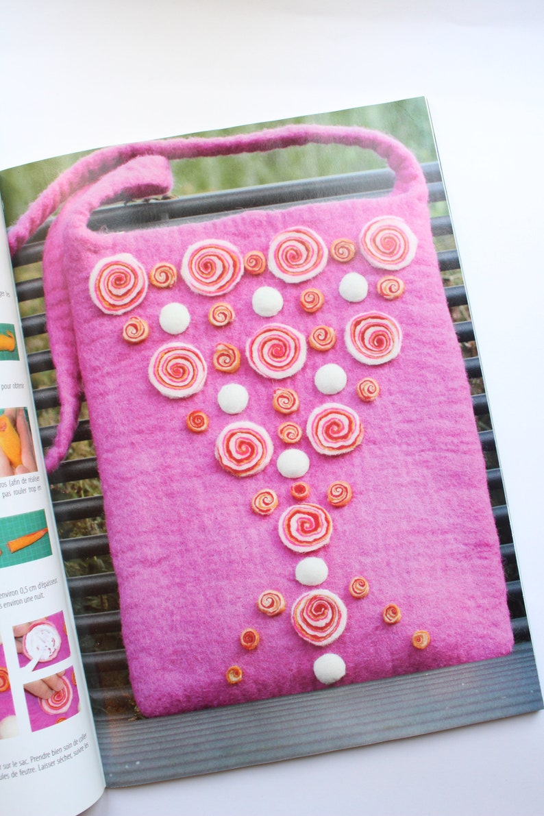 May include: A pink felt bag with a white strap and a design of white and pink felt circles arranged in a triangular pattern.