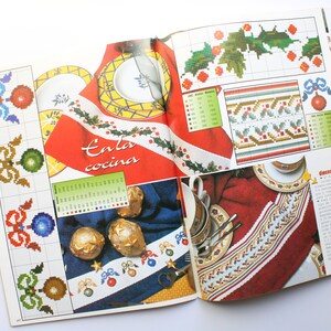 May include: A magazine page with cross-stitch patterns for holiday decorations. The patterns include holly leaves, bows, and ornaments. The text on the page reads "En la cocina".